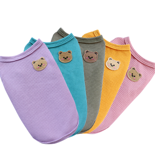 Five sleeveless waffle-textured cat vests in lavender, teal, olive green, mustard yellow and pink, each featuring a small bear-face patch.